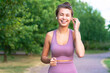 Portrait of beautiful, happy young woman talking through bluetooth headphones while at sports jog. A girl laughs, listens to music with wireless headphones.