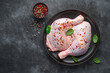 Two chicken thighs sprinkled with pepper and basil on a dark background.