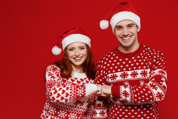 Wall Mural - Young smiling happy fun couple friends two man woman 20s in sweater hat give fistbump isolated on plain red background studio portrait. Happy New Year 2022 celebration merry ho x-mas holiday concept.