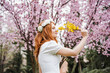 © Westend61 - Beautiful woman smelling yellow flower while standing in front of almond tree at park