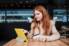 Redhead Woman Holding Credit Card While Using Digital Tablet At Cafe
