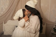 © Тамара Киреева - a beautiful dark-haired girl in a knitted sweater hat is standing on the bed with her little daughter in a hat and a Latin hugging Christmas
