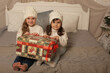 © Тамара Киреева - little girls in winter knitted hats and white sweaters are sitting on the bed holding gift boxes