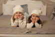© Тамара Киреева - beautiful little girls in winter knitted hats and white sweaters are lying on the bed