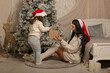 © Тамара Киреева - a beautiful dark-haired girl in a knitted sweater and knee socks is sitting by the bed giving each other gift boxes at the Christmas tree