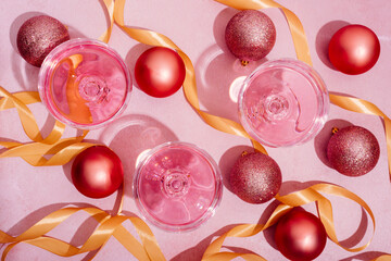 Pink champagne in luxury crystal glasses and christmas baubles with golden ribbon decor. Top view. New year eve celebration and nightclub party with girly drink toast.