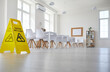 © Studio Romantic - White school, college or university classroom with row of desks and chairs where janitorial or cleaning service worker placed plastic sign with figure that slips and falls and words Caution Wet Floor