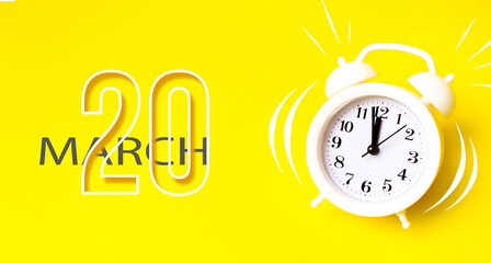 March 20th. Day 20 of month, Calendar date. White alarm clock with calendar day on yellow background. Minimalistic concept of time, deadline. Spring month, day of the year concept.