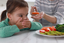 Mother Feeding Her Daughter Indoors, Closeup. Little Girl Refusing To Eat Vegetables