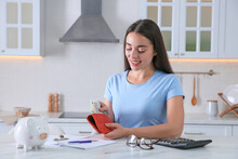 Young Woman Counting Money At Table In Kitchen