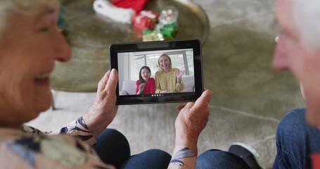 Wall Mural - Senior caucasian couple smiling and using tablet for christmas video call with family on screen