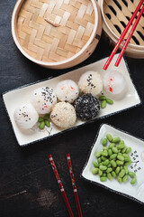 Wall Mural - Plate with onigiri or japanese rice balls, flatlay on a dark-brown stone background with a bamboo steamer, vertical shot