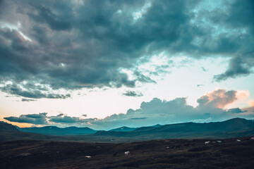 Wall Mural - surrealist mountain scenery with horses and golden dawn light in cloudy sky. scenic mountain landsca