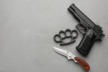 Wall Mural - Black brass knuckles, gun and knife on light grey stone background, flat lay. Space for text