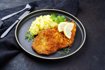 Traditionelles frittiertes Schnitzel mit Kartoffelsalat und Zitronenscheiben serviert als close-up auf einem Modern Nordic Design Teller mit Textfreiraum