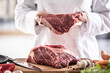 © weyo - Fresh red meat cut in hands of a chef with chunk of meat on a wooden board