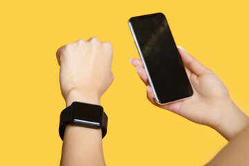 Wall Mural - Devices for sport. Young woman with smart watch and smartphone with blank black screen, yellow background