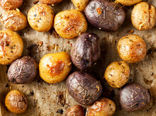 Top View Close Up Image Showing Fresh Oven Baked Potato Medley With A Variety Including Purple Heart Potatoes. Potatoes Are Cooling On Baking Paper. Concept Image For Healthy Snack Or Side Dish