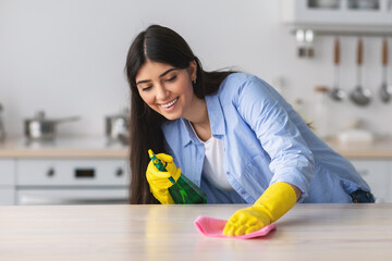 Wall Mural - Cheerful young woman cleaning table with cloth