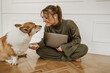© Look! - Cute young caucasian lady is playing with her dog at home while working at laptop. Girl with gathered blond hair in glasses, headphones and suit. Lovely pet concept.