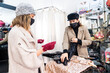 © unai - Caucasian employee with a mask from a luxury clothing store trying on showing a sequin dress to a client, security measures in the coronavirus pandemic, covid-19