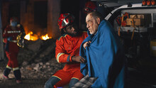 African American Bearded Man In Paramedic Uniform Asking Questions To Senior Man Wrapped In Blanket After Accident At Night