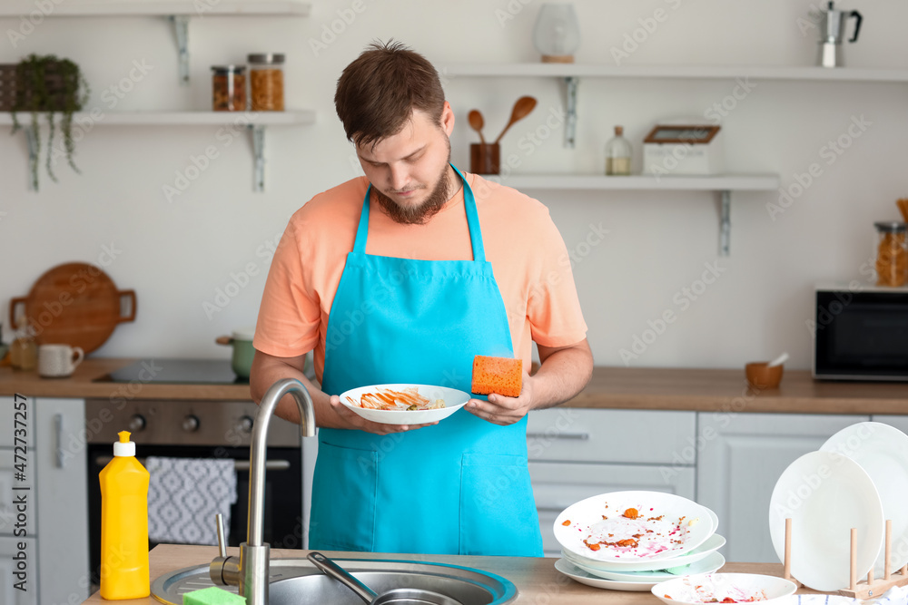 Young man with sponge washing dishes in kitchen