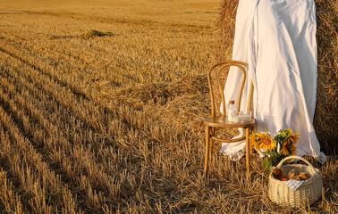 Wall Mural - Romantic picnic with tasty food and wine decorated with sunflowers, chair and white fabric in harvested field