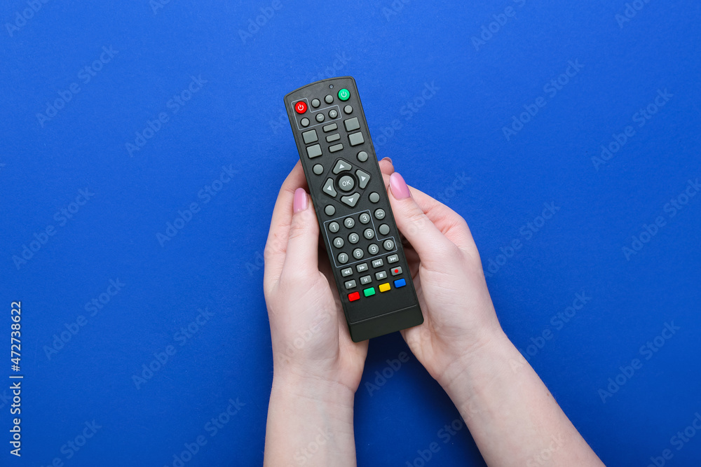 Woman holding TV remote controller on blue background, closeup