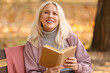 © Pixel-Shot - Mature woman reading book in autumn park
