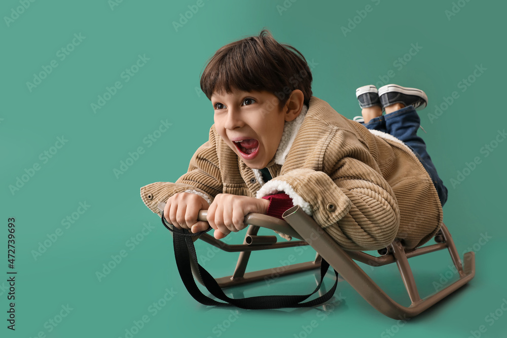 Sledding little boy on color background