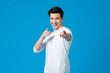 © Atstock Productions - Young happy handsome Caucasian man smiling and pointing fingers at you in isolated light blue background