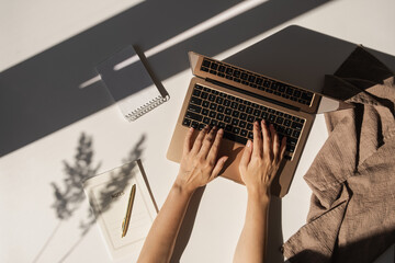 Flatlay of person hands working on laptop computer. Aesthetic bohemian home office workspace. Work at home. Notebook, pampas grass sunlight shadow on table. Flat lay, top view