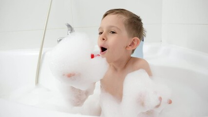 Wall Mural - Smiling little boy playing with soap foam in bath and blowing it from hands.Concept of hygine, children development and fun at home