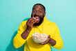 © deagreez - Photo of excited positive guy film addicted eat pop corn wear sweater isolated over cyan color background