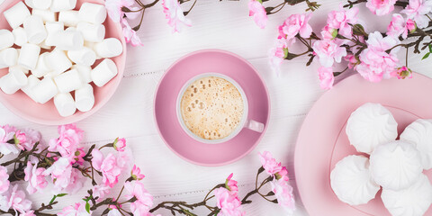 Romantic spring still life. Coffee cup with marshmallow in the morning for breakfast. Cherry blossom on white wooden background. Flat lay. Pastel pink card. Food background. Dessert with floral decor.