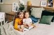 © Sviatlana - Mom and daughter read fairy tales in the bedroom on the bed on Christmas or New Year's Eve. Holiday atmosphere, Christmas mood