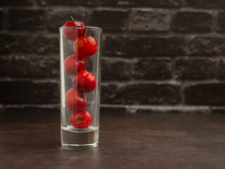 Wall Mural - Ripe red acerola cherries in glass on a cement floor with a black brick wall background