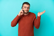 © luismolinero - Young Brazilian man using mobile phone isolated on blue background having doubts while raising hands