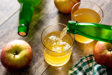 Pouring apple cider drink into a glass on wooden rustic table