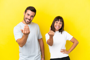 Canvas Print - Young couple isolated on yellow background inviting to come with hand. Happy that you came