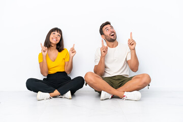 Wall Mural - Young couple sitting on the floor isolated on white background pointing with the index finger a great idea