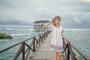 Wall Mural - Vacation on tropical island. Young woman in hat enjoying sea view from wooden bridge terrace, Cloud 9 Surf Spot, Siargao Philippines.