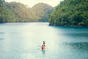 Wall Mural - Summer holidays vacation travel. SUP Stand up paddle board. Young women sailing together on beautiful calm lagoon.