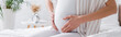 © LIGHTFIELD STUDIOS - partial view of pregnant woman touching belly in bedroom, banner.