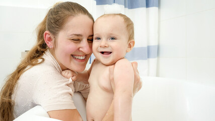 Wall Mural - Smiling baby boy washing in bath with foam with mother. Concept of children hygiene, healthcare and development at home