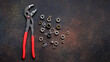 Top view of adjustable universal pliers for repair and assorted nuts on dark rusty background with copy space
