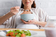© LIGHTFIELD STUDIOS - cropped view of happy pregnant woman eating oatmeal near tray with salad.