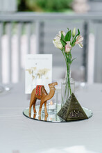 Preparing For An Open-air Party Decorated With Fresh Flowers Served Tables Table Number Decoration Details Egypt-theme Table Decoration Souvenir Figure Of A Wooden Camel And Egyptian Pyramid Statue