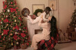 © Тамара Киреева - a beautiful brunette girl with long hair in pink pajamas is sitting on a chair covered with a plaid plaid by the Christmas tree fireplace holding a little daughter